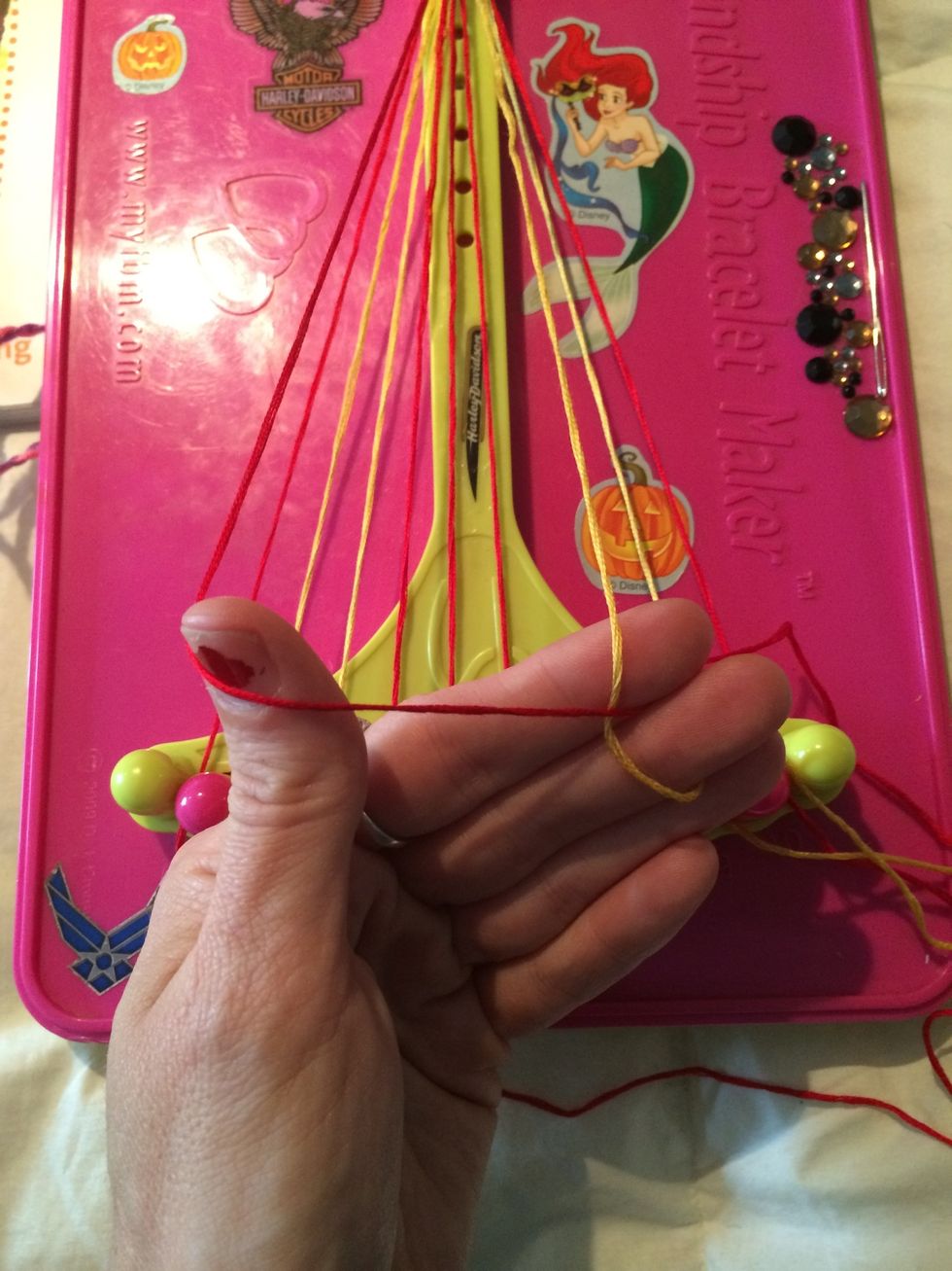 Continue onto the gold string. And then knot over the remaining strings.