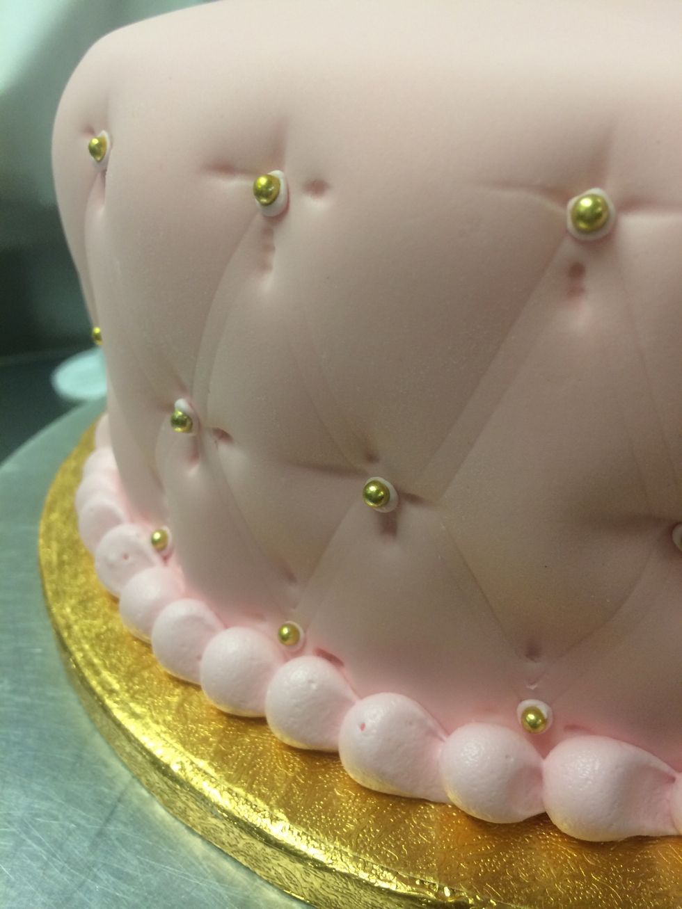 Continue to fill each center stitch with a tiny pink dot of royal icing and gold bead. Using a larger round tip, pipe a boarder around the bottom and board of the cake.