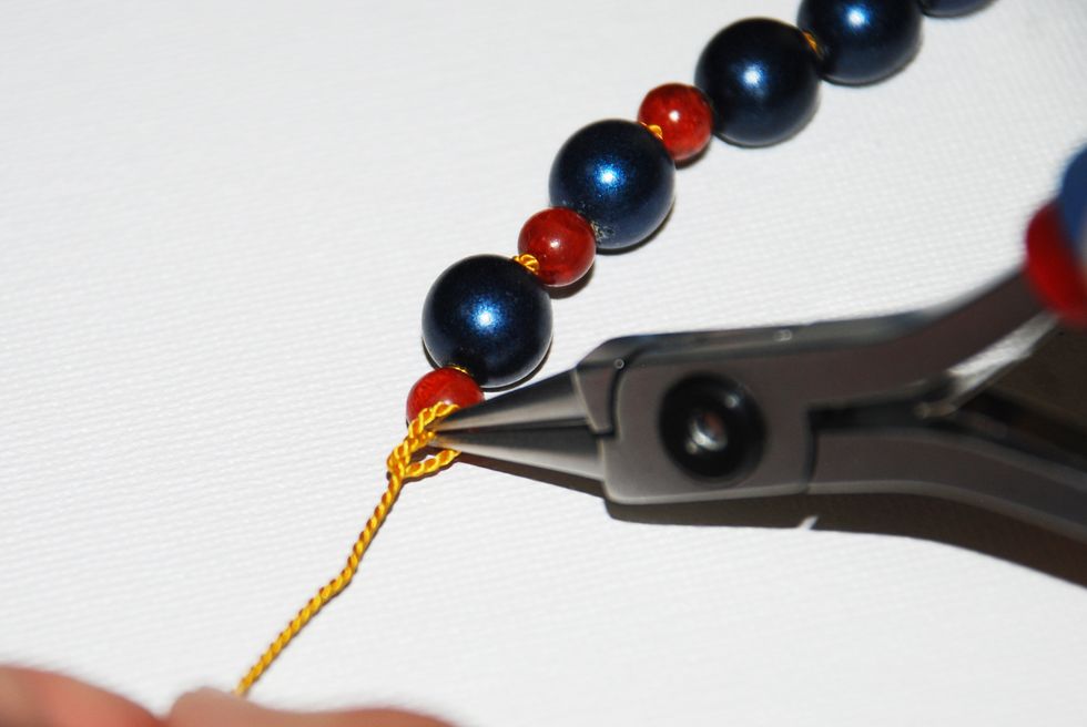 Continue to hold the thread with your round nose pliers, while you pull the long end of the thread to tighten the knot over the tip of the pliers.