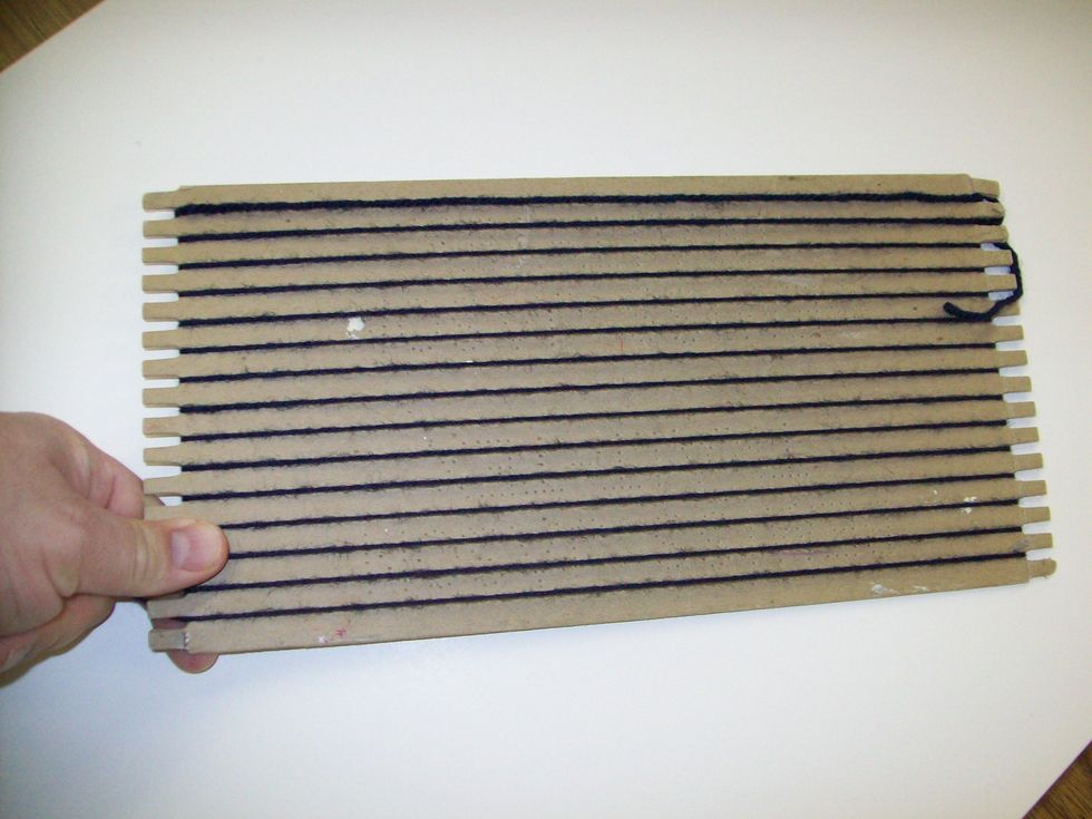 Continue wrapping the yarn around the loom between the teeth until you go between the last teeth on the bottom of the loom. Make sure you have about 8 inches of yarn hanging over the edge.