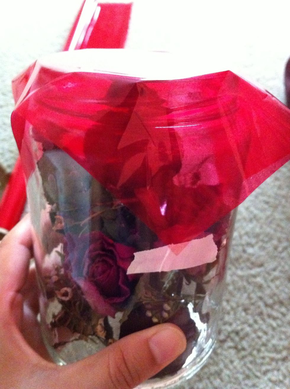 Cover the jar with cello wrap, have someone help you on this part, you're gonna need to tie the ribbon on. I'm home alone so I figure to just tape all 4 corners, so it'll be still.