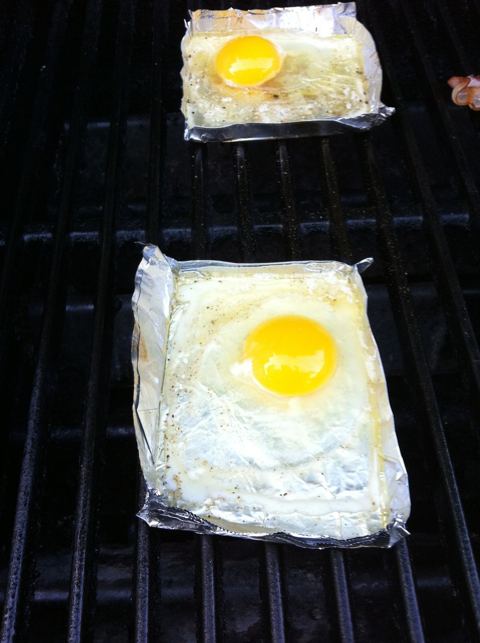 Crack one egg into each foil tray. Close cover and grill until desired doneness. Until white is no longer transparent and yolk is starting to set. Around 4 minutes. Season with salt and pepper.