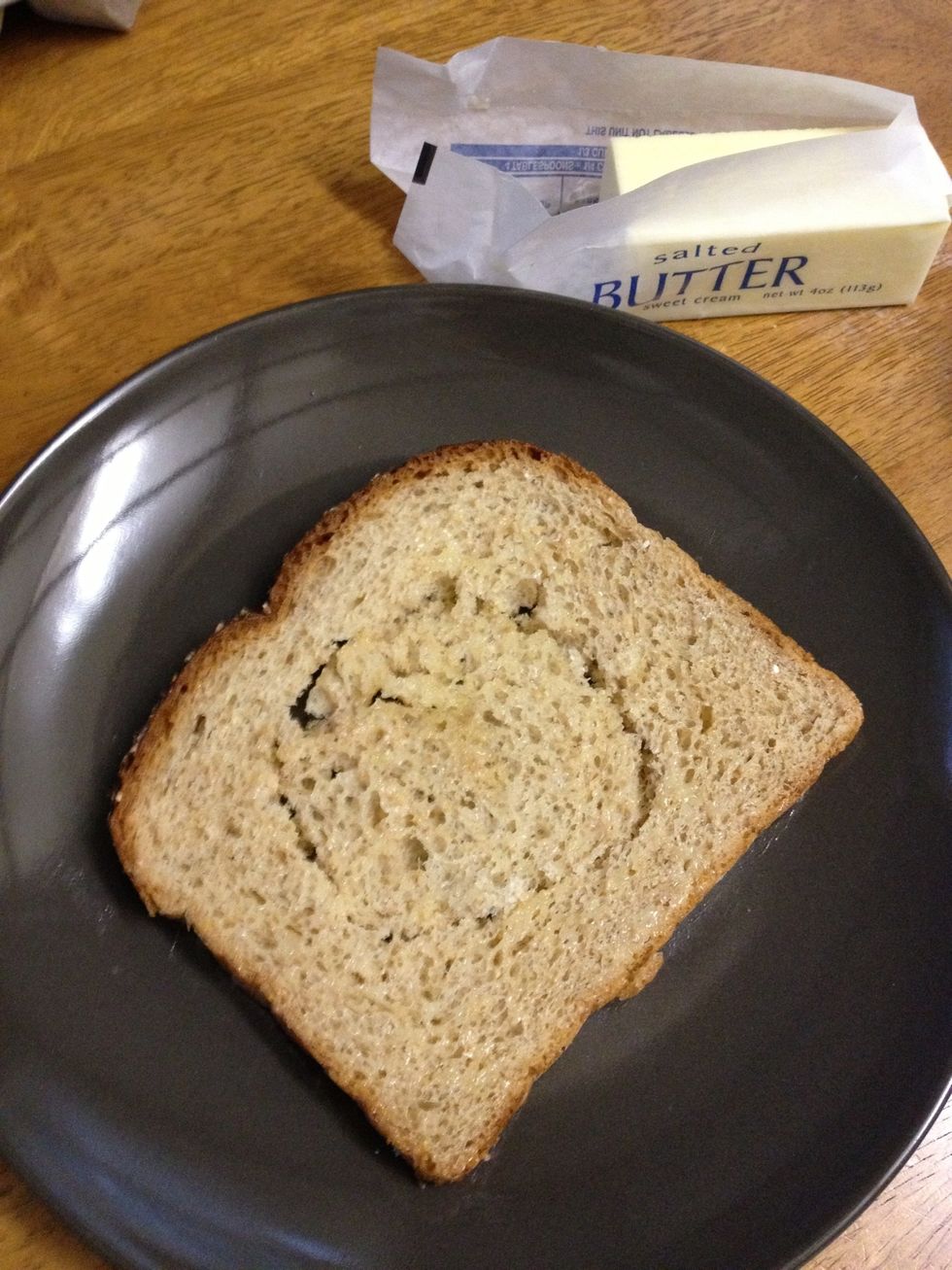 Cut a hole in the middle of the bread and spread melted butter on each side. A small glass can also be used to create the hole.