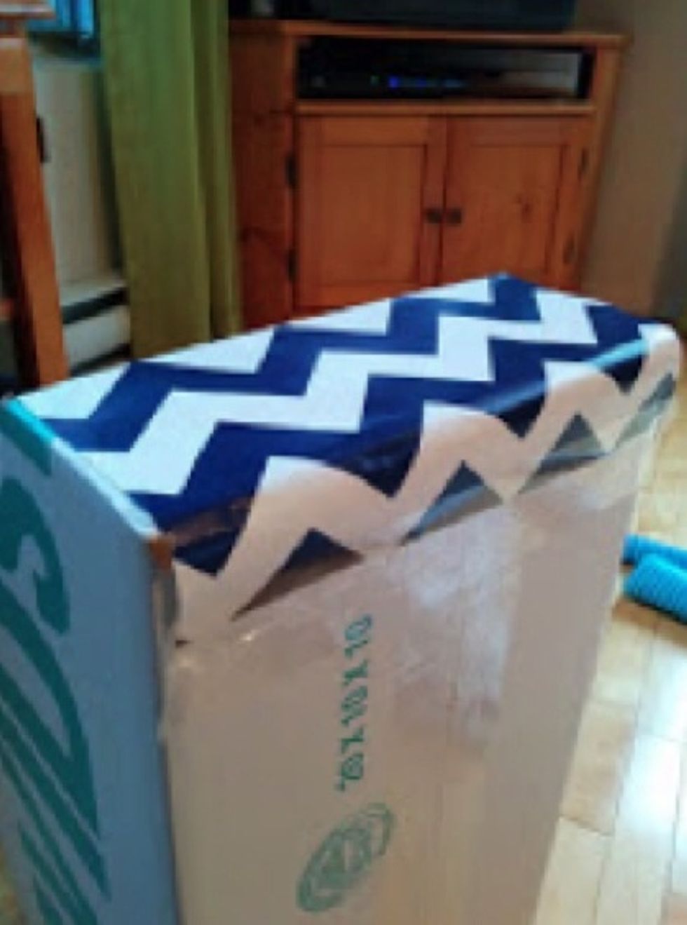 Cut a large 155cm x 25cm sheet of wrapping paper. Using scotch tape, tape the end of the wrapping paper to the back of the box.