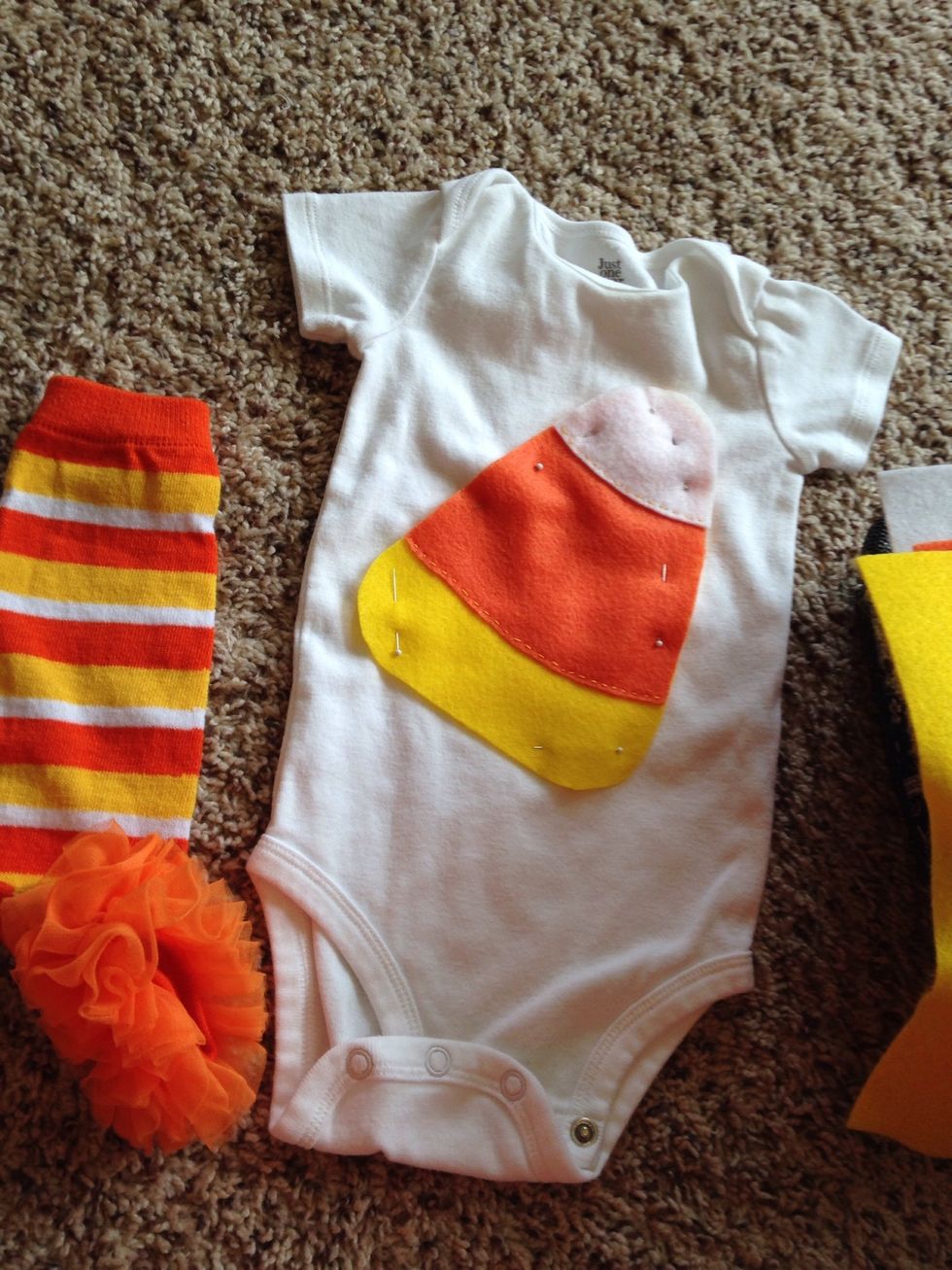 Cut a long piece of thread and put it through the needle tying a knot at the end. Bring thread through the inside of the onesie through the bottom of the orange felt