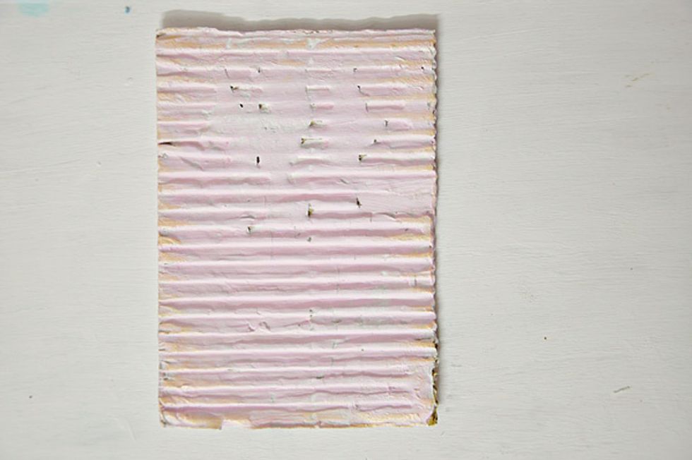Cut a piece of corrugated cardboard, approximately to serve as photo mat. Paint with gesso and very light pink acrylic paint. Ink the edges with distress ink and gold ink.