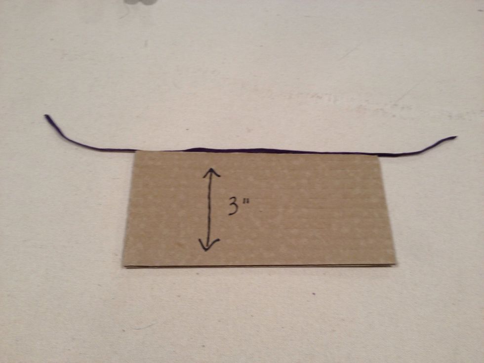Cut a piece of yarn about 8" long and position it along the edge of the cardboard as shown.