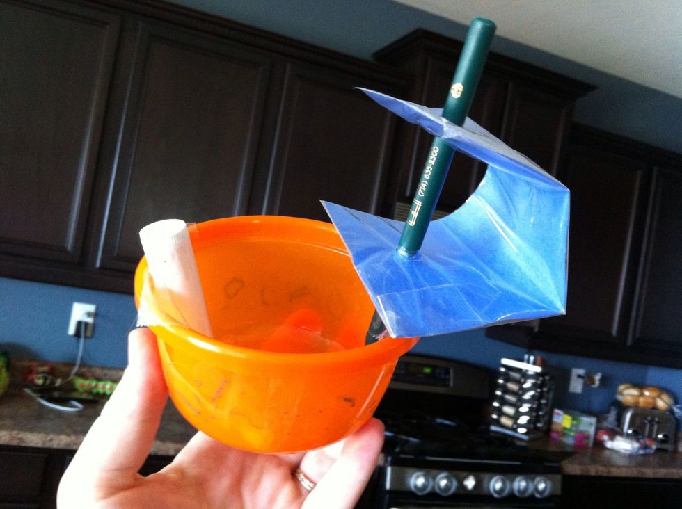 Cut a rectangle of paper (~ 2"x8"). Put paper in ziplock, fold over & tape (to make sail water tight). Poke a pen through sail. Tape pen & Chapstick to Tupperware boat (Chapstick= counterweight).
