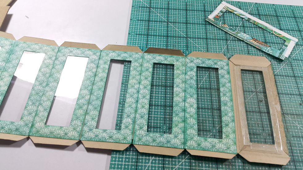 Cut acetate 8pcs of 1-5/8"x4-1/8" and adhere at the back of the window, left one for future steps. Cut papers of the same size as the chipboard panels, cover both insides and outsides.
