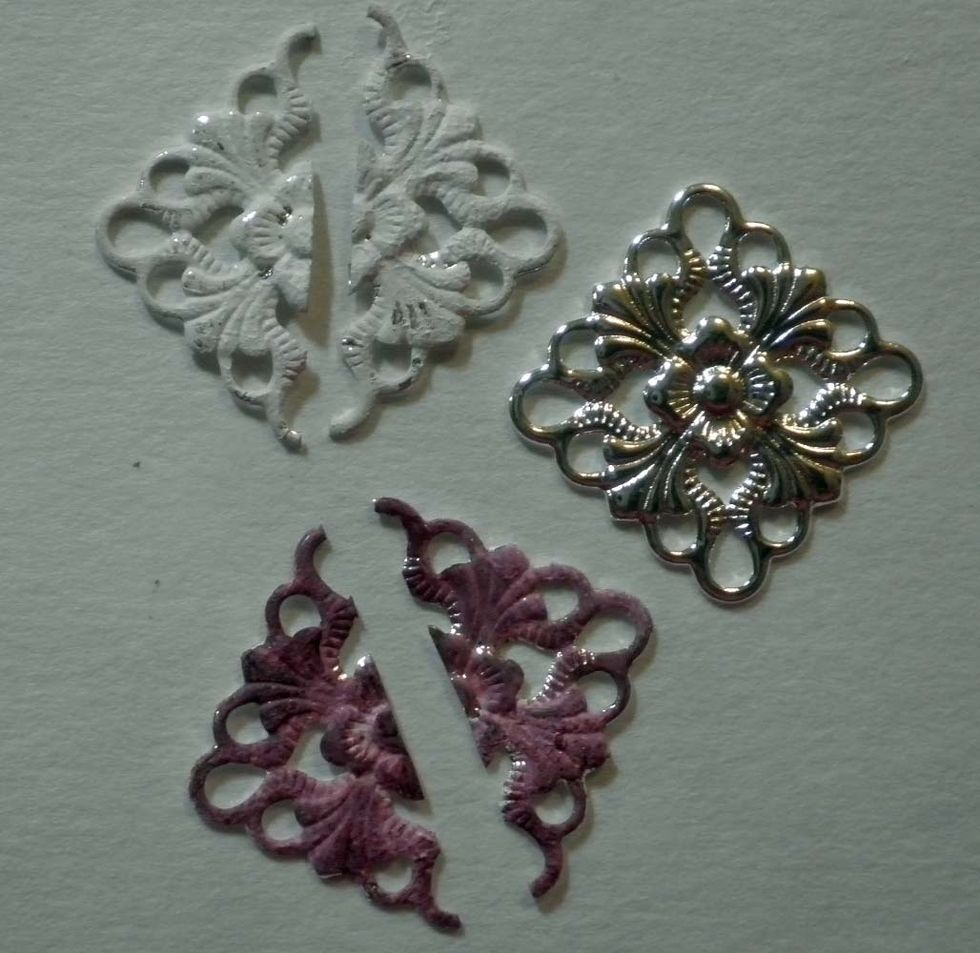 Cut apart two metal filigree charms, as shown. Sponge white gesso over each corner piece, then add ColourArte Radian Rain Wine & Roses dauber color atop. Let dry.
