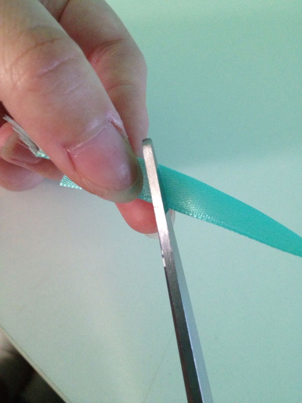 Cut at an angle like so. Tilting the scissors towards your hand (I'm right handed and held the ribbon with my left).
