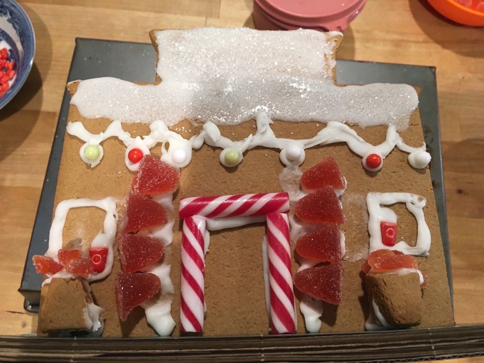 Cut more gumdrops into slices and put them on top of the plant holders with frosting. Put candy cane sticks as the door. Then add a knob with frosting and bead candies.
