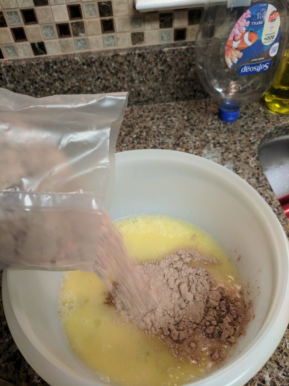 Cut open the chocolate syrup pouch and the dry brownie mix and pour into the liquid mixture in the mixing bowl.