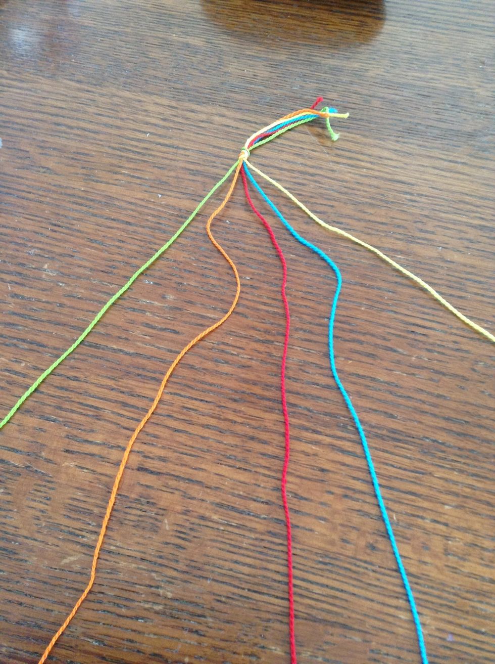 Cut out 5 different color strings, arms length, and tie a knot at the top to connect them. Lay them out on a table or flat surface.
