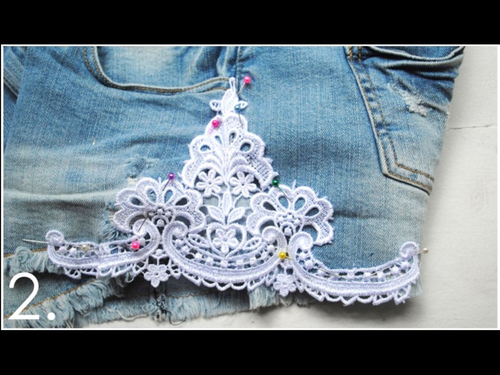 Cut out a piece of lace in your desired size. You don\u2019t have to use all of the trim \u2013 feel free to cut off the edges to get the right shape! Then pin the lace in place on top of the shorts.