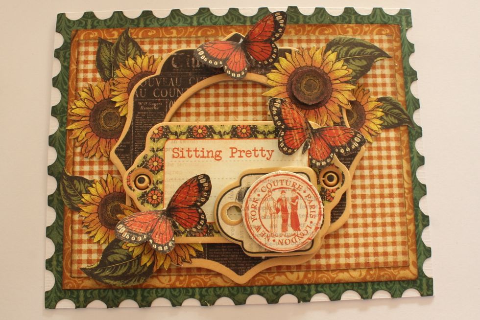 Cut out three butterflies from one of the sheets in the Botanicabella Deluxe Kit and attach them to the card. Also add a chipboard label and a die-cut on top of the chipboard piece.