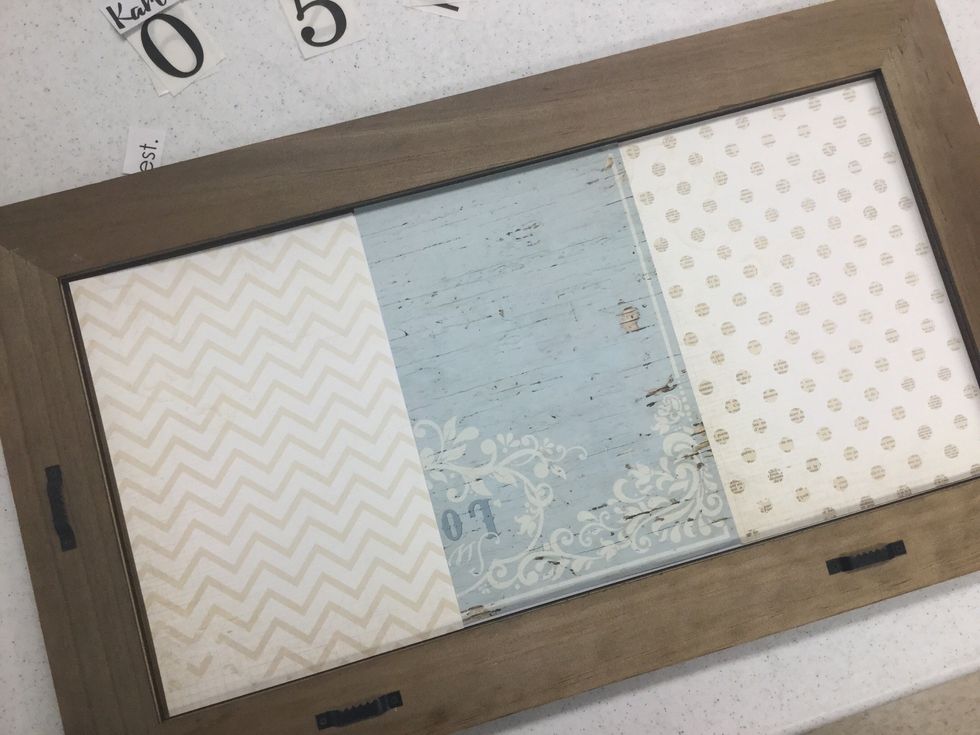 Cut scrapbook paper to fit. We cut our paper 6" wide and 9" high. Take the backing off the frame and lay papers over the mat openings. You may adhere the pieces in place, but it's not necessary.