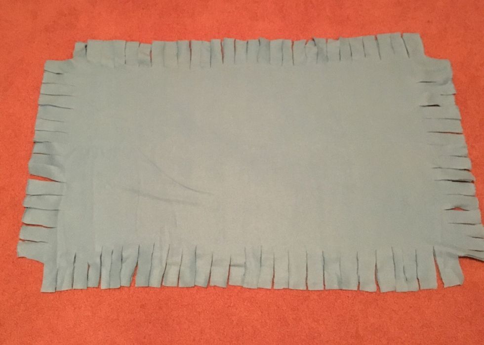 Cut strips in the edges of the blanket about 1 1/2 inches apart, and about 3-5 inches long. The longer and skinnier they are, the easier they are to tie, but not too long or too skinny.