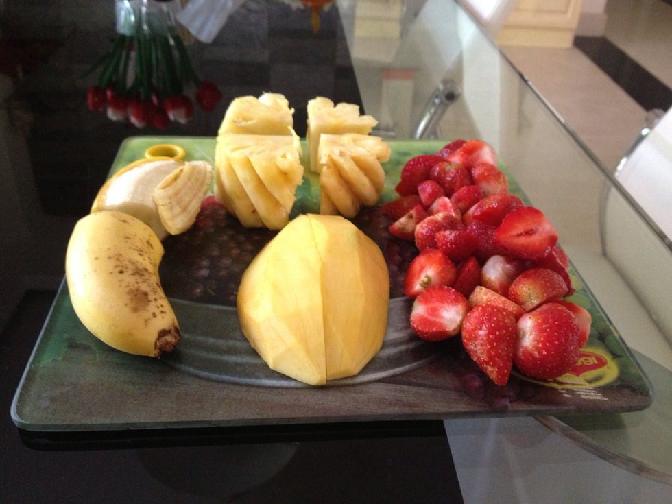 Cut the banana, mango, and frozen strawberries in half. I do advise you to dip the knife in hot water first when cutting the strawberries since they are stiff.  Chop the pineapples to small chunks.