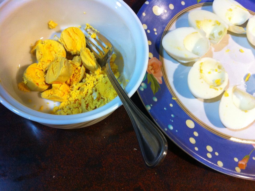 Cut the eggs in half and remove the yolks with a spoon. Place yolks in a separate bowl and start smashing with a fork.