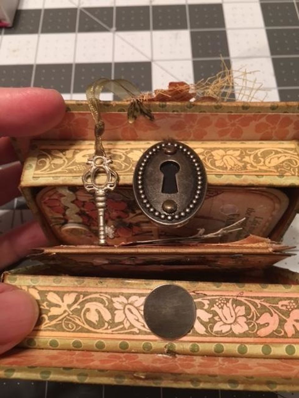 Cut the prongs off of two brads and glue the brad heads to the holes of the key hole. Attach a large magnet paper snap on  the opposite side of the box on the outside as shown in this photo.