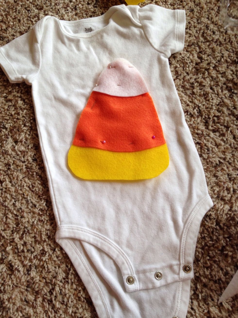 Cut the white felt to fit at the top of the candy corn and pin it to the onesie. Trim the pieces to fit correctly