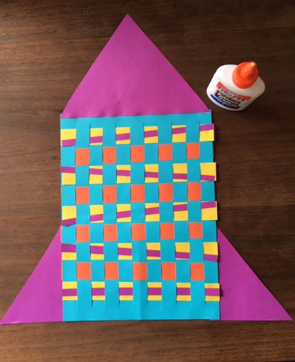 Cut triangle shape from paper with scissors and glue to the top of weaving. Use the two smaller triangles you cut off for fins. Glue to each side at the bottom of the rocket.