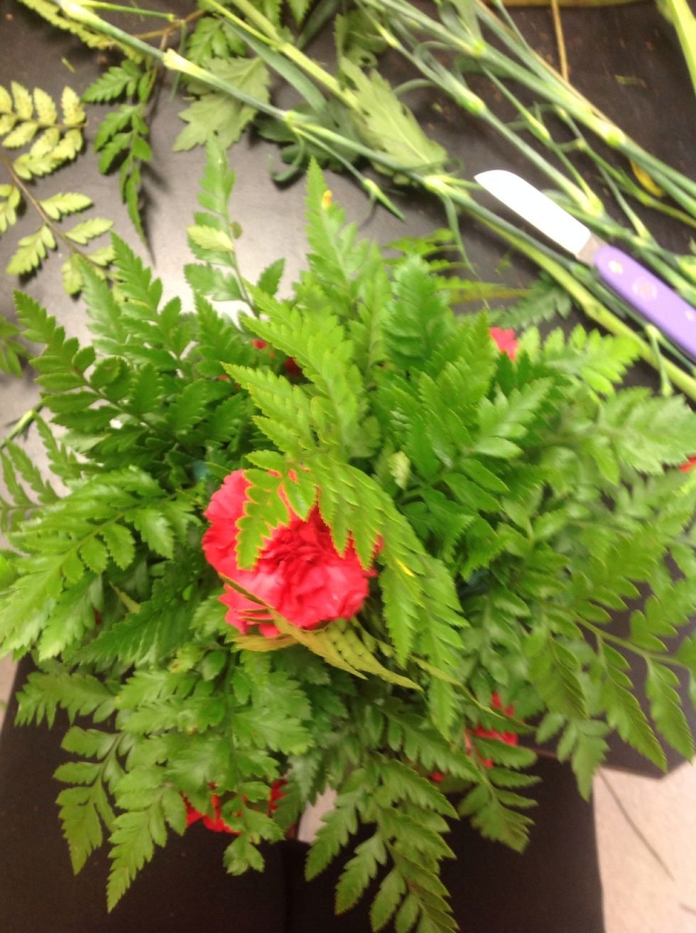 Cut your main flower to be a half an inch or so shorter than your leather leaf. Place your first flower in between the two center pieces of leather leaf. Then add 5 flowers evenly around the bottom.