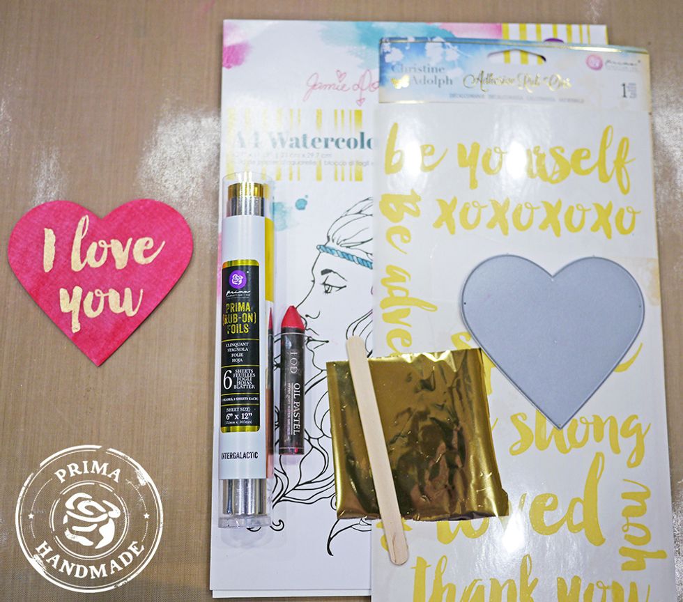 Die-cut a heart with watercolor paper. Apply adhesive rub-on \u201cI love you\u201d sentiment to die-cut heart, then apply gold foil on top. Color with Red Oil Pastel and spread color with a wet brush. Dry.
