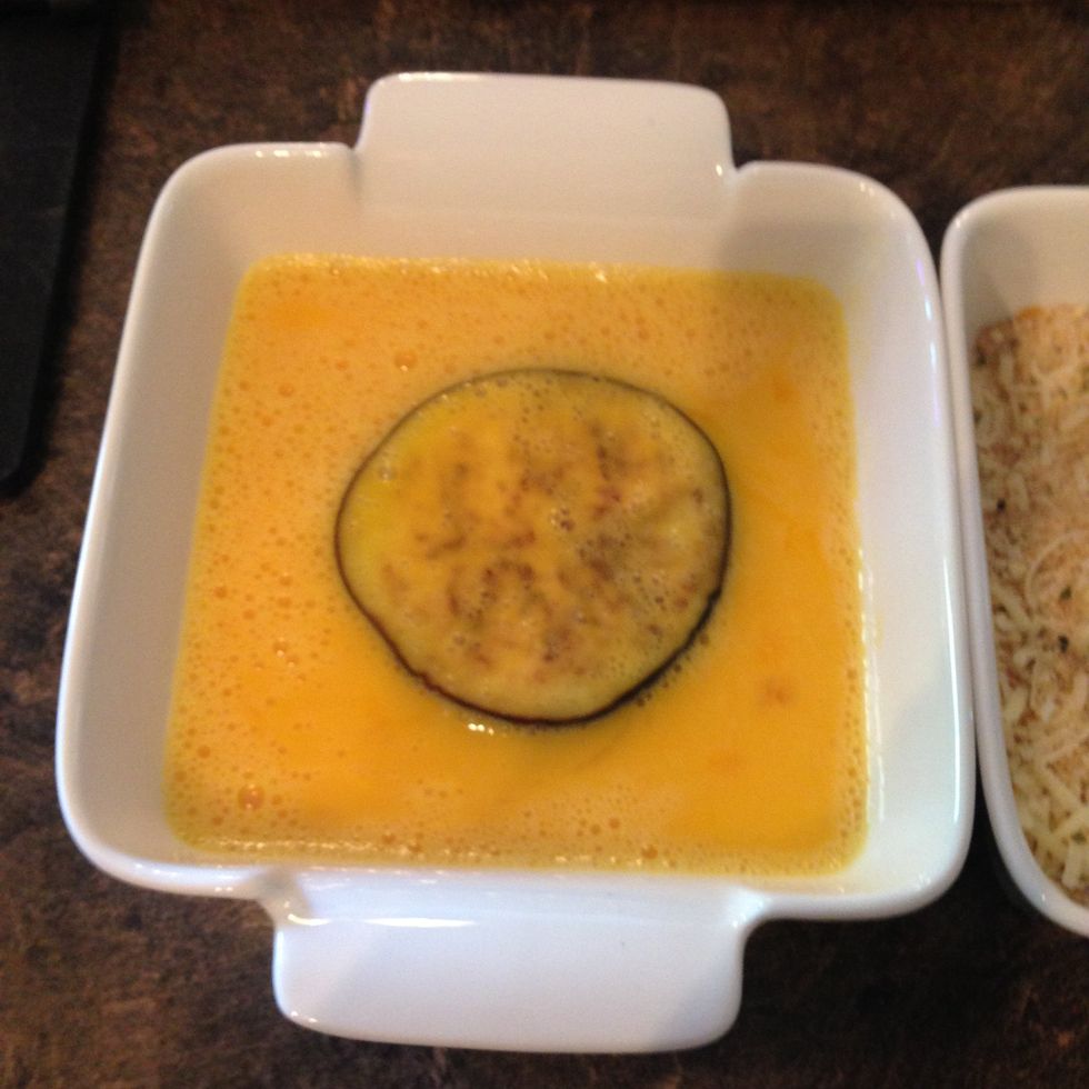Dip a slice of eggplant in the egg.