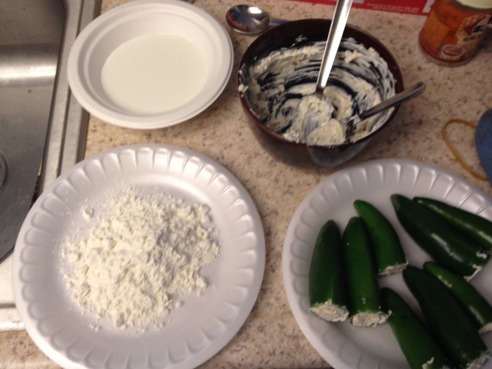Dip stuffed jalape\u00f1o into the milk. Then drop into the flour. Let them dry.