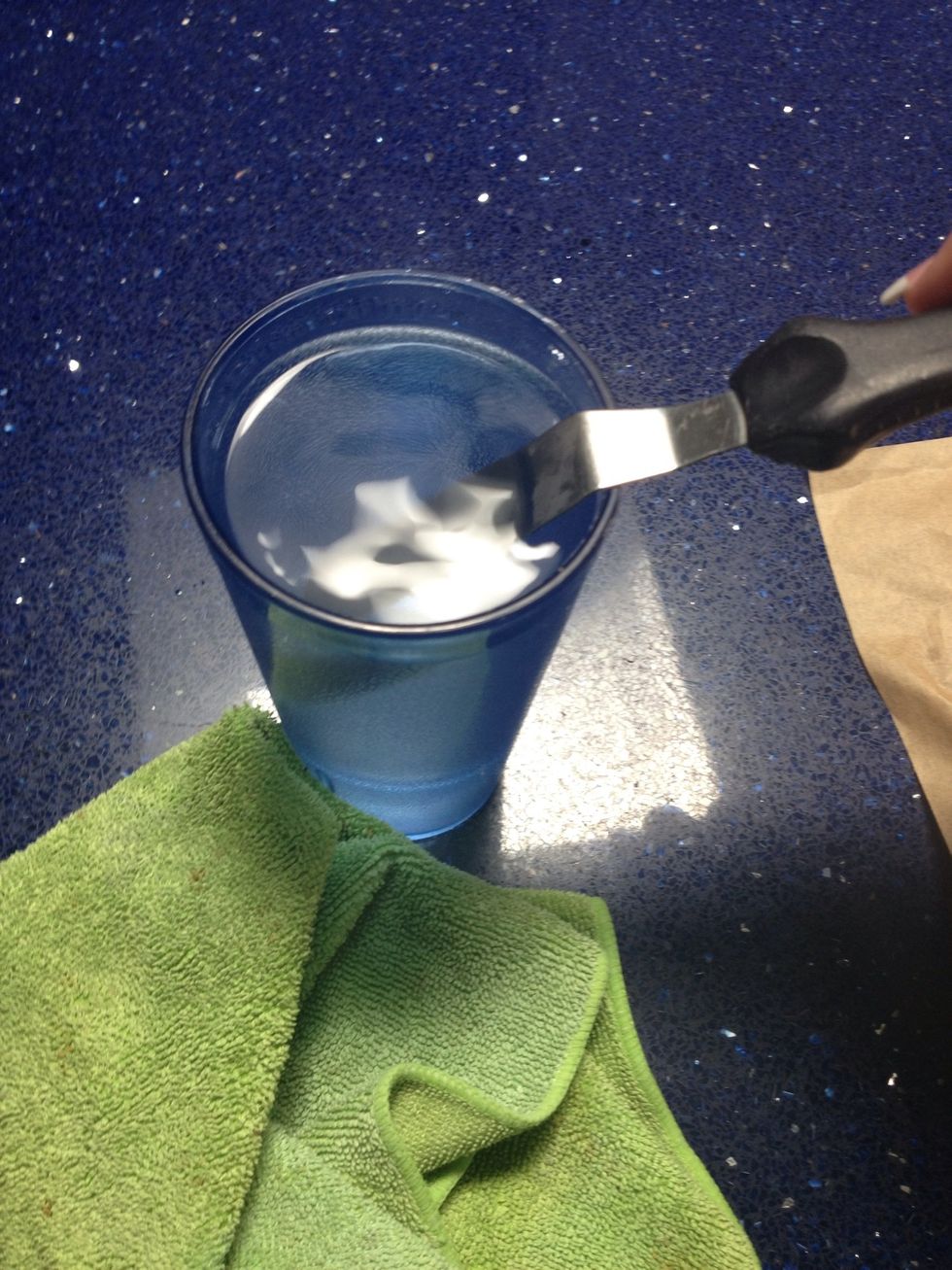 Dip your icing spreader in the cup of boiling water, like so.