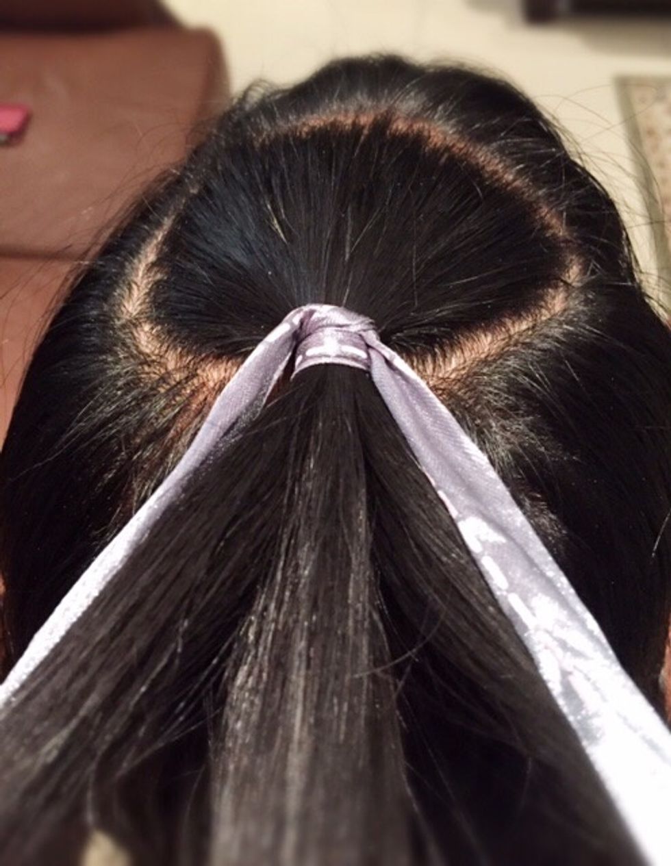 Divide the hair tied by the ribbon into three equal sections. Bring the ends of the ribbon down into your left and right sections, keep your ribbon there throughout the process.