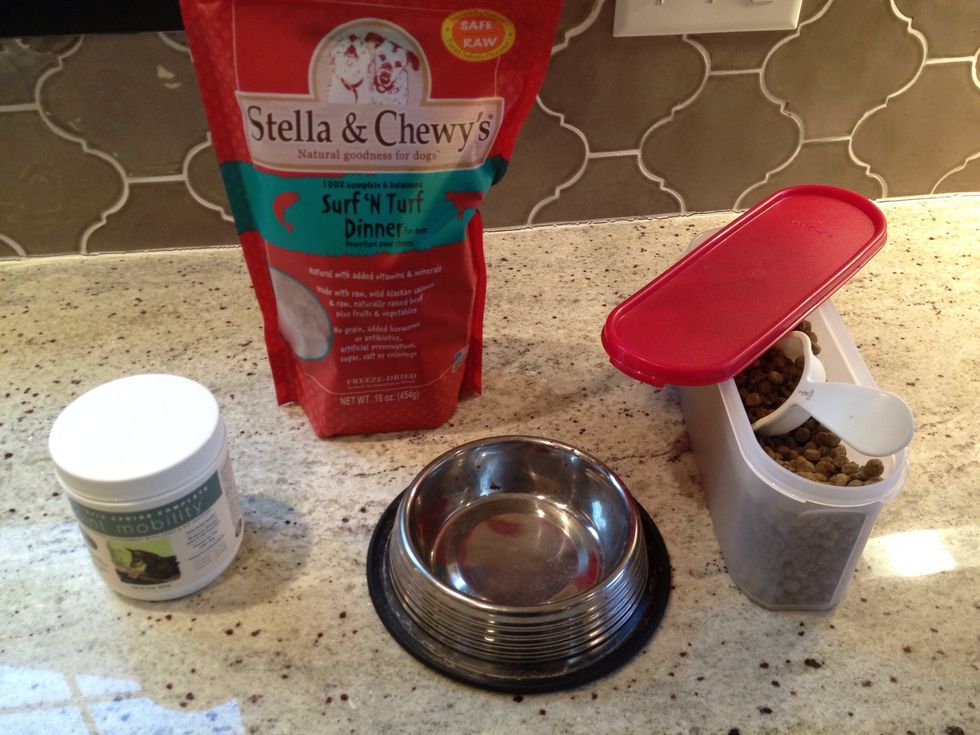 Dog food bowl in the middle. 50/50 blend of dog food on the right. Freeze dried dog food top middle. Joint mobility supplement on the left.