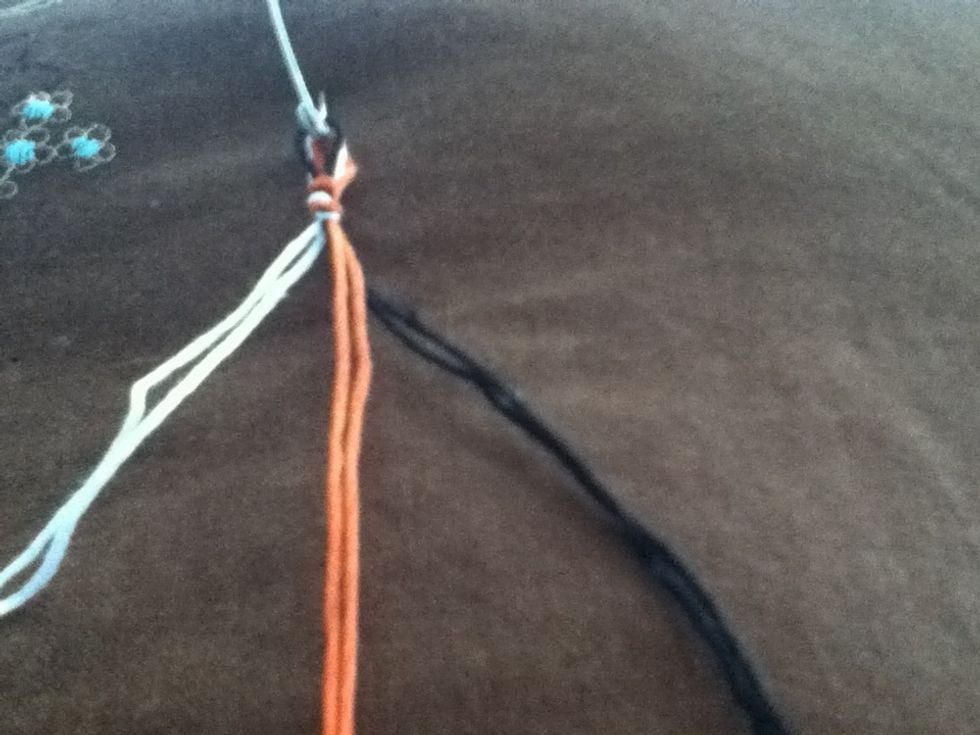 Double up your threads and tie a knot leaving a loop. Use the safety pin to attach to a pillow or other work surface. Divide thread by color. My orange thread is the center/unseen thread.
