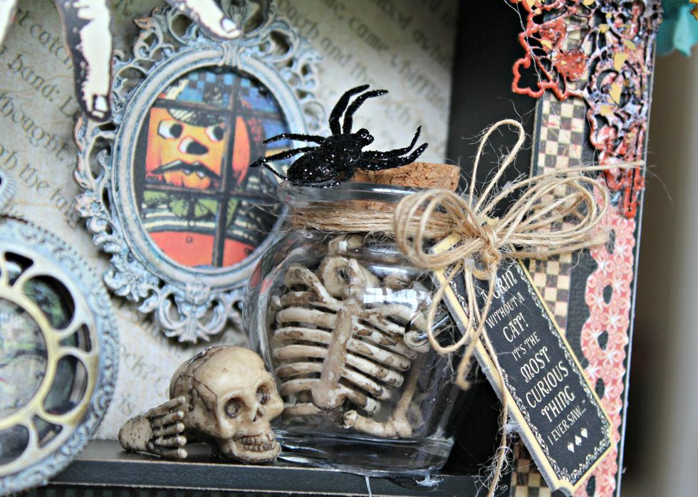 Dry brush frame with Titan Buff paint. Adhere to image from pattern paper. Add to front of top space with pop dots. Fill jar full of skeleton bones. Adhere to shelf of top space.