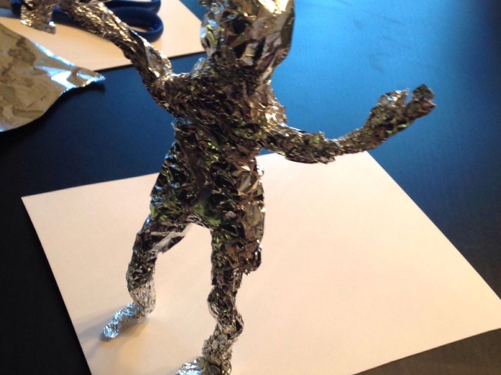 Du kanske beh\u00f6ver mer aluminiumfolie p\u00e5 benen, kroppen och armarna. Figuren kanske beh\u00f6ver en accessoar ocks\u00e5? Limma fast figuren p\u00e5 en bit kartong med limpistolen.