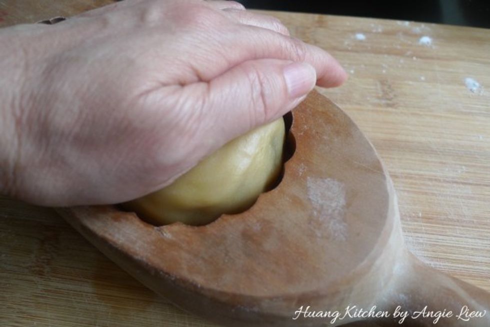Dust lightly the dough ball with flour, put into the lightly floured mooncake mould and press hard and flatten the dough so that the shape conform to the mould.