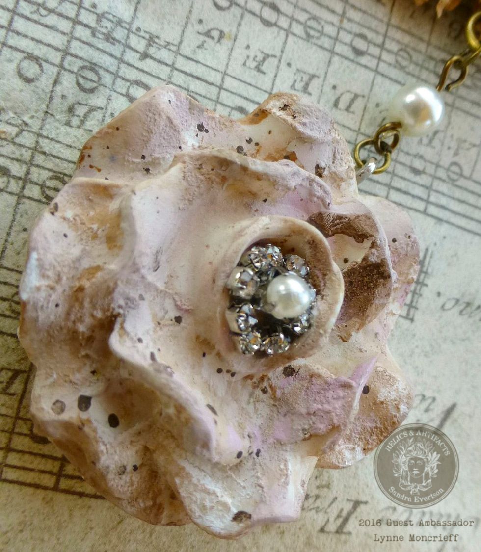 Embellish the center of the resin flower with rhinestone chain and pearl embellishment, adhered with E6000. Attach the flower to the large heart with jewelry findings and pearls.
