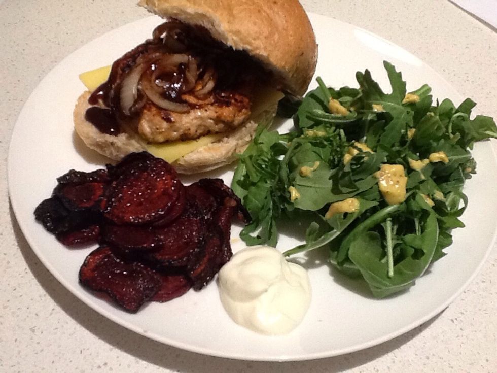 Ensemble the burger with the bun, the chicken pattie, onion rings, BBQ sauce and a slice of cheese. Put the salad, the beetroot chips along with the burger on a plate.