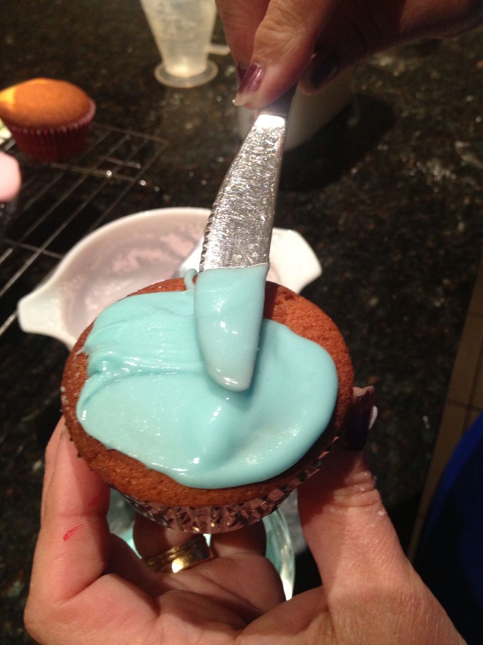 Evenly spread blue icing over one cupcake with the flat part of a bread knife to receive a smooth texture