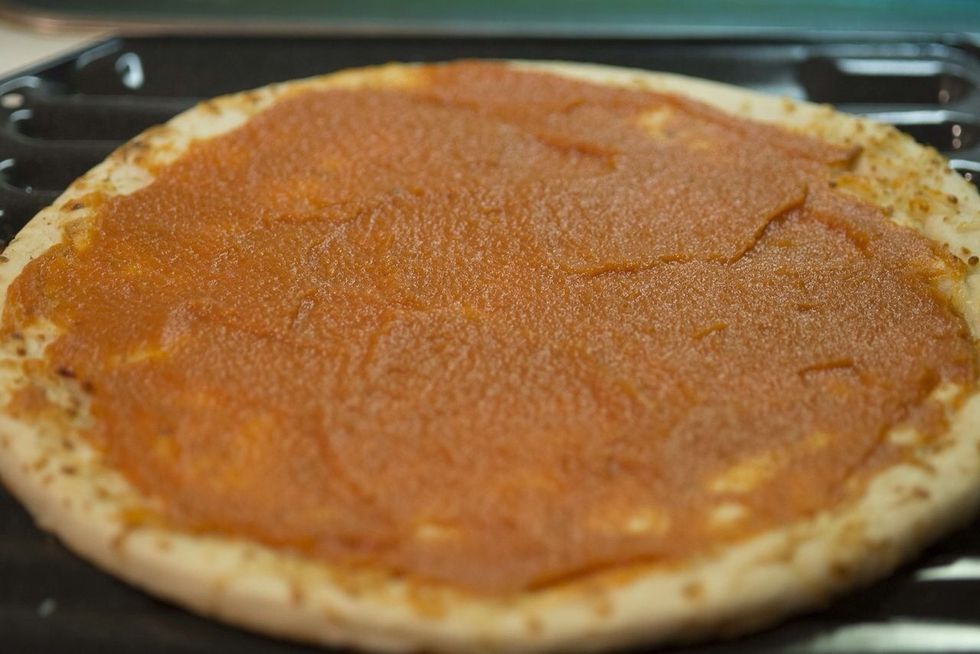 Evenly spread the sauce onto the whole wheat pizza crust. Be sure to leave a lip around the edge of the dough. It will keep your oven clean and will make eating the pizza with your hands easier.