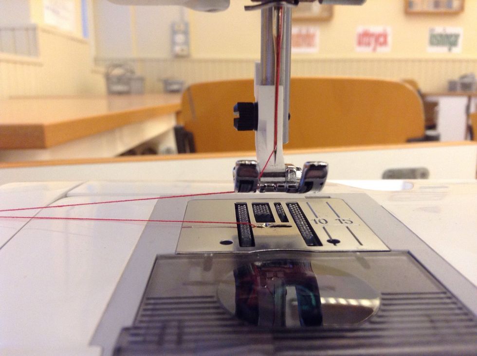 F\u00f6r tr\u00e5darna genom sk\u00e5ran p\u00e5 pressarfoten. B\u00e5da tr\u00e5darna ska nu vara mellan pressarfoten och stygnpl\u00e5ten.