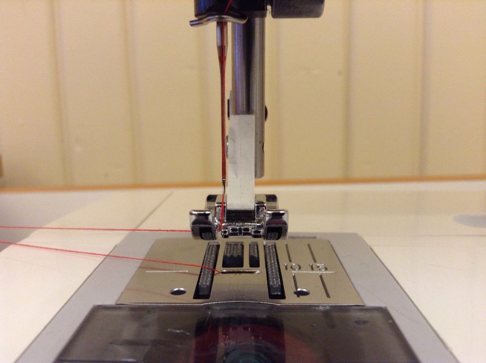 F\u00f6r tr\u00e5darna genom sk\u00e5ran p\u00e5 pressarfoten. B\u00e5da tr\u00e5darna ska nu vara mellan pressarfoten och stygnpl\u00e5ten.