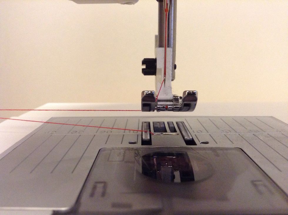 F\u00f6r tr\u00e5darna genom sk\u00e5ran p\u00e5 pressarfoten. B\u00e5da tr\u00e5darna ska nu vara mellan pressarfoten och stygnpl\u00e5ten.