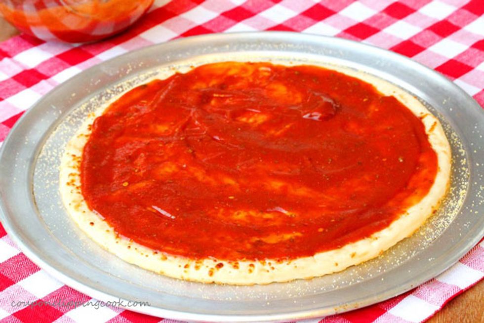 Fill the ladle with tomato sauce and spread the tomato sauce around the dough make sure that there's no chunks of sauce but make sure there's no spots without tomato sauce