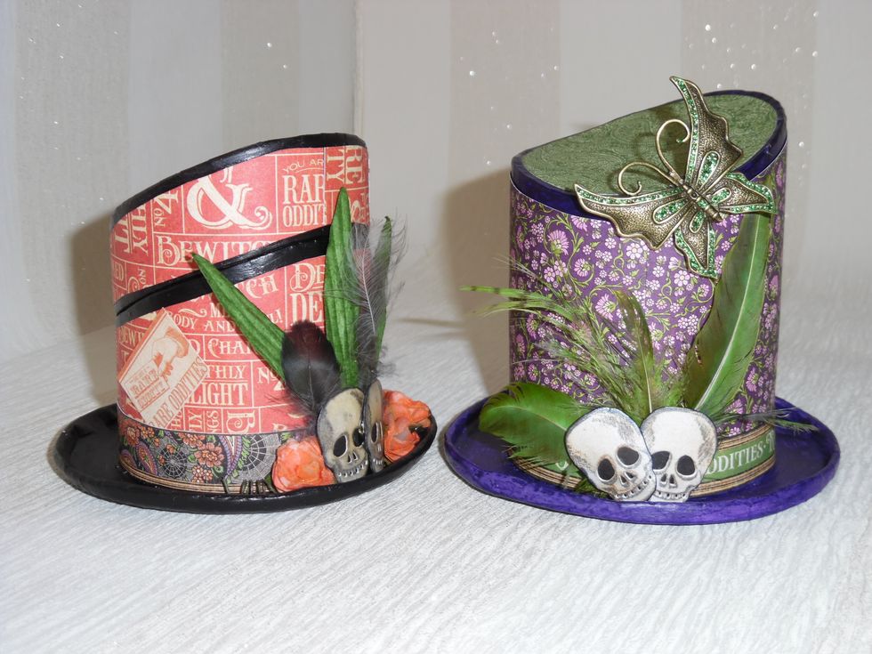 Finally add embellishments to dress the hats. Die cut skulls, feathers from my garden (coloured with ProMarkers). Paper roses and paper leaves. Metal butterfly from my stash with added glitter.