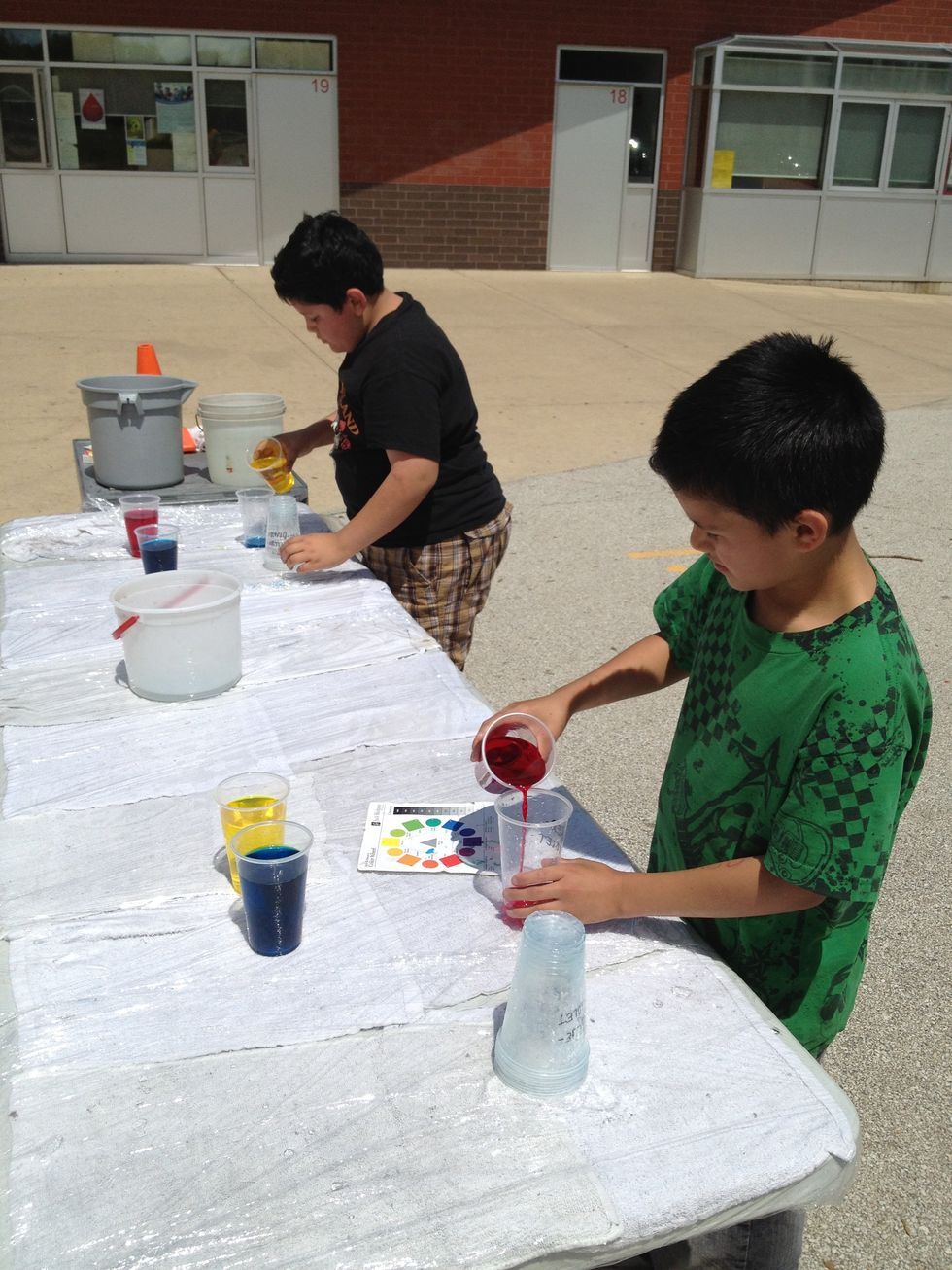 Finally, the student pours their mixture into the empty tertiary color cup they chose. They check their color to see if it's correct. If needed, they can spill out and start again.