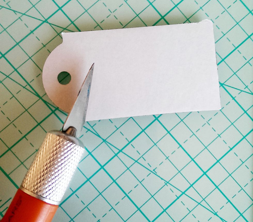 Find the brown tag chipboard, and with a knife, slice the backing about \u00be of the way up. Leave the backing on the upper part, since it will hang off the tag.