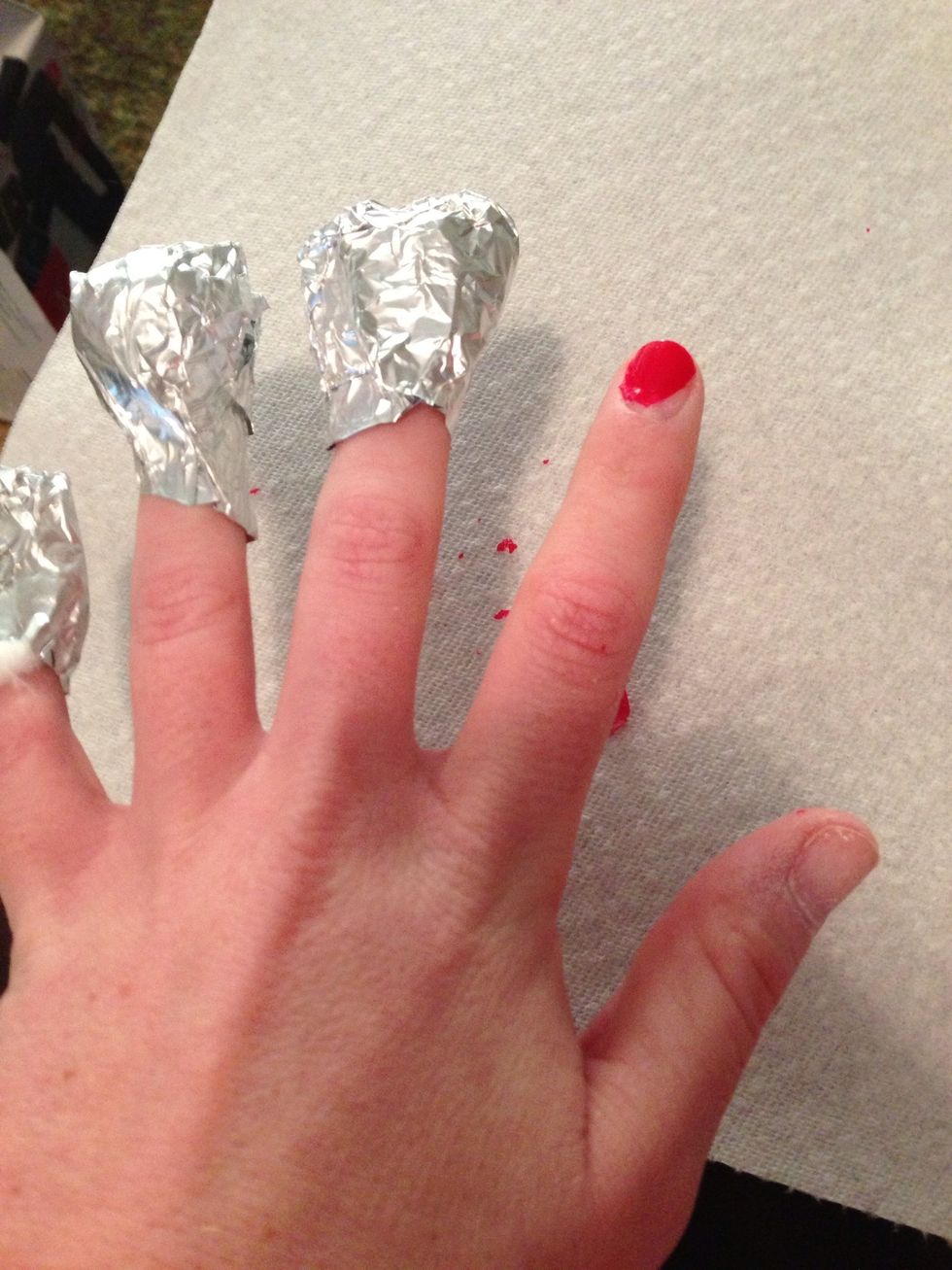 Finger by finger, pull tin foil off and scrape polish off. Should come off fairly easy, if not just put the tinfoil and cotton ball back on for a few minutes.